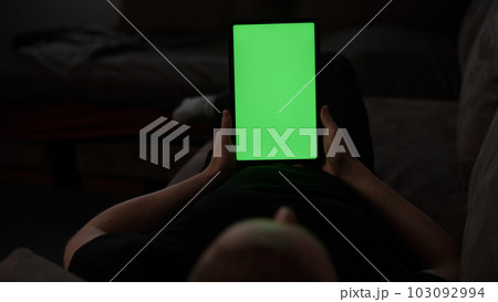 Man at home lying on a couch with tablet pc with green screen Man at home lying on a couch with tablet pc with green screen 103092994