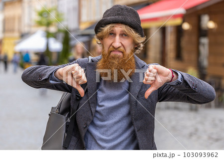 Upset young man showing thumbs down sign, disapproval, dissatisfied bad work, mistake in city 103093962