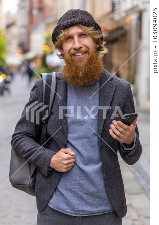 Young man use smartphone typing text messages browsing internet finishing work looking at camera Young man use smartphone typing text messages browsing internet finishing work looking at camera 103094025