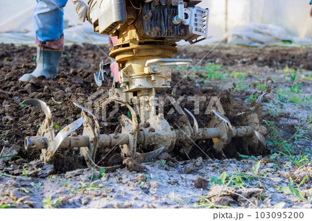 There is farmer plowing ground with tiller block using motor cultivator in garden There is farmer plowing ground with tiller block using motor cultivator in garden 103095200