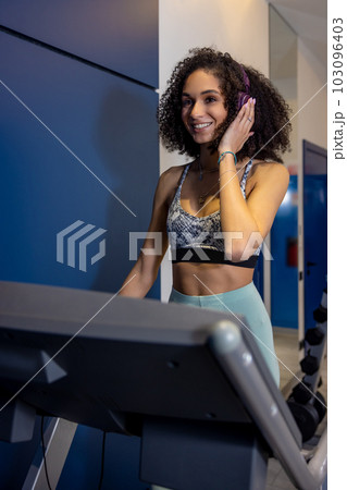 Curly-haired young woman on a treadmill looking contented 103096403