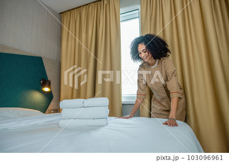 Curly-haired young woman making bed on a hotel room 103096961