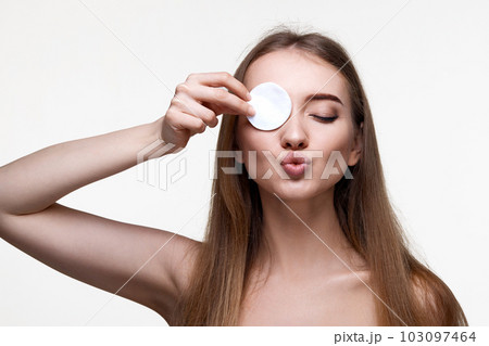 woman with naked shoulders close one eye with white cotton pad woman with naked shoulders close one eye with white cotton pad 103097464