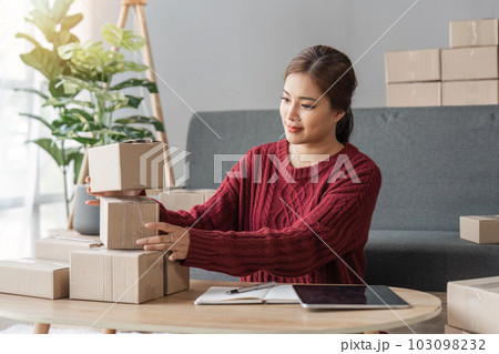 Happy young asian woman startup small business freelance holding parcel box and computer laptop and sitting sofa, Online marketing packing box delivery concept Happy young asian woman startup small business freelance holding parcel box and computer laptop and sitting sofa, Online marketing packing box delivery concept 103098232