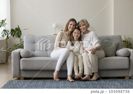 Three generations of women sit on sofa looking at camera Three generations of women sit on sofa looking at camera 103098736