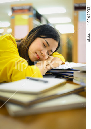 Tired exhausted young student sleeping on the table in library with pile of books. Education, prepare to exam, lesson Tired exhausted young student sleeping on the table in library with pile of books. Education, prepare to exam, lesson 103099334