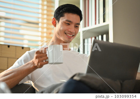 Pleasant man freelancer drinking hot coffee and checking news or email on laptop. People, technology and lifestyle concept 103099354