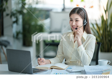 Portrait of happy smiling female customer support phone operator at workplace. Asian Portrait of happy smiling female customer support phone operator at workplace. Asian 103100964