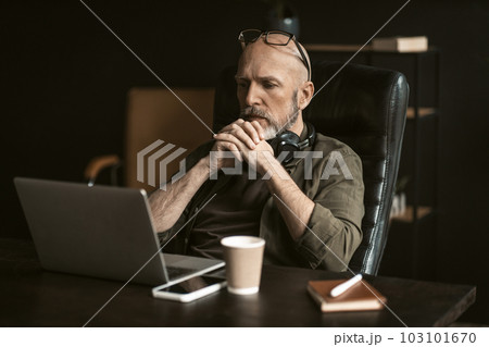 Dedicated elderly worker in loft office environment. With puzzled expression on his face, he sits attentively in front of a computer, deeply engaged in solving a complex problem. . High quality photo Dedicated elderly worker in loft office environment. With puzzled expression on his face, he sits attentively in front of a computer, deeply engaged in solving a complex problem. . High quality photo 103101670