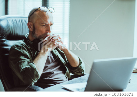 Middle-aged man fully focused on work he looks intently at computer on table. Deep in thought, he reflects on task or problem at hand, demonstrating his analytical and strategic thinking skills 103101673
