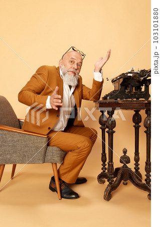 Portrait of bearded, mature, bald man in elegant, classical suit sitting near typewriter and spreading hands. Professional crisis Portrait of bearded, mature, bald man in elegant, classical suit sitting near typewriter and spreading hands. Professional crisis 103101880