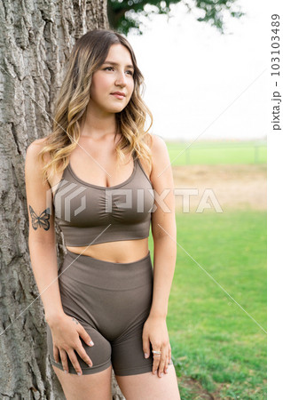 Caucasian woman in fitness clothes standing in front of tree trunk and posing 103103489