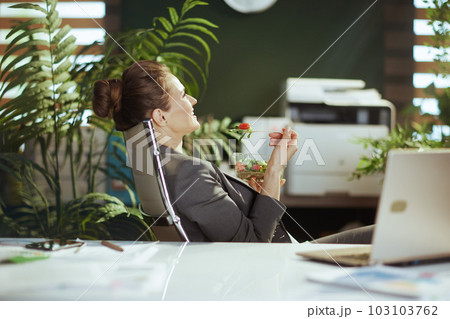 relaxed female employee in green office eating salad 103103762