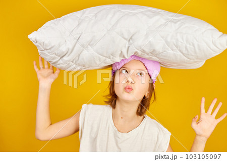 Funny teenage girl in white pyjamas with a violet sleeping mask hold pillow 103105097
