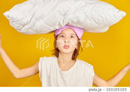 Funny teenage girl in white pyjamas with a violet sleeping mask hold pillow 103105105