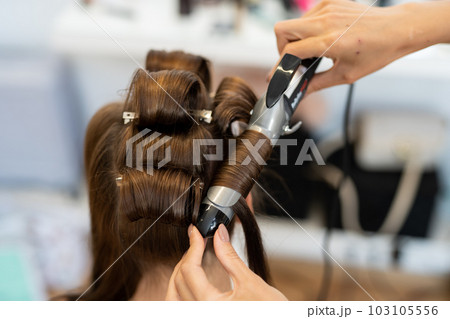 The hairdresser curls the model's hair. Curling iron for curling hair close-up. 103105556
