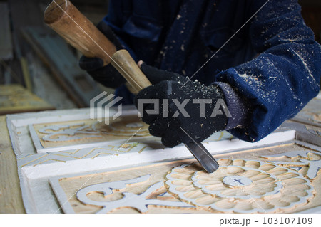 Close Up of Man Hands carving on wooden furniture. Carpenter using tool making Artistic Wood Carving. Producing an Ornament on Wood with Chisel and Hammer on a Panel of Wood . High quality photo 103107109