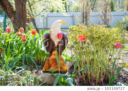 A flower bed in the yard of a cottage with an eagle figurine. 103109727