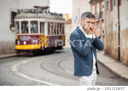An adult man plays the harmonica on the street with a tram behind his back 103115657