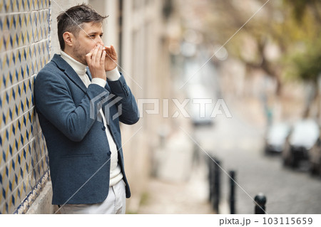 A man stands against the wall and plays the harmonica in the street 103115659