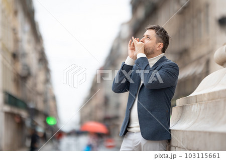 A man in a blue jacket plays the harmonica on the street looking up 103115661