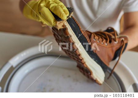 A person is cleaning men's suede casual boots with brush, sponge and spray. Shoe shine and care. Footwear moisture and dirt protection. 103118401
