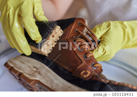 A person is cleaning men's suede casual boots with brush, sponge and spray. Shoe shine and care. Footwear moisture and dirt protection. 103118431