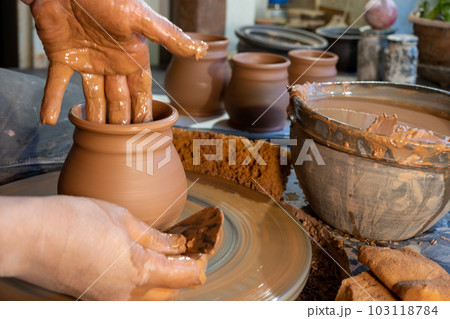 ceramics, workshop, ceramic art concept - close-up of man's hands forming a new vessel, man's fingers working with potter's wheel and raw edge, frontal close-up. 103118784