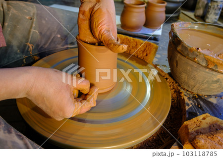 ceramics, workshop, ceramic art concept - close-up of man's hands forming a new vessel, man's fingers working with potter's wheel and raw edge, frontal close-up. ceramics, workshop, ceramic art concept - close-up of man's hands forming a new vessel, man's fingers working with potter's wheel and raw edge, frontal close-up. 103118785