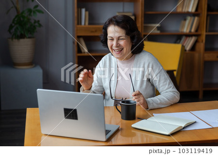 Happy middle aged senior woman sit with laptop talk on video call with friends family. Laughing mature old senior grandmother having fun talking speaking with grown up children online Happy middle aged senior woman sit with laptop talk on video call with friends family. Laughing mature old senior grandmother having fun talking speaking with grown up children online 103119419