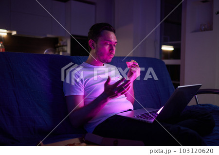 Handsome young man eating unhealthy food while watching movie at night. Handsome young man eating unhealthy food while watching movie at night. 103120620