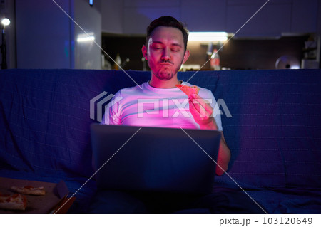 Handsome young man eating unhealthy food while watching movie at night. 103120649