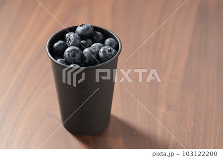 Blueberries in black paper cup on walnut table Blueberries in black paper cup on walnut table 103122200