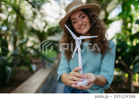 Young woman in botanical garden holding model of wind turbine, concept of green energy. 103124386