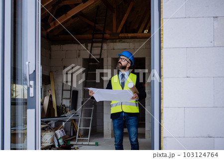 Mature businessman controlling blueprints from unfinished house. 103124764