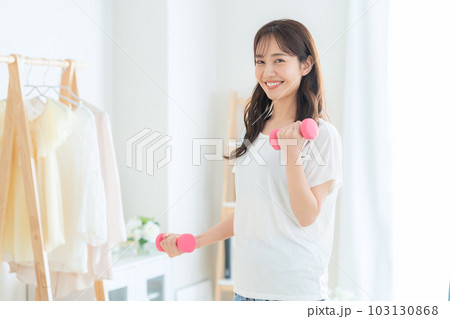 リビングでダンベルを使って筋トレをする若い女性 103130868