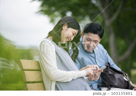 公園でスマートフォンを見る若い夫婦 公園でスマートフォンを見る若い夫婦 103135801