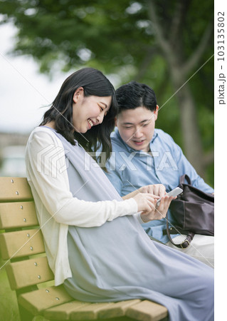 公園でスマートフォンを見る若い夫婦 公園でスマートフォンを見る若い夫婦 103135802
