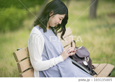 公園でスマートフォンを見る妊婦 公園でスマートフォンを見る妊婦 103135805