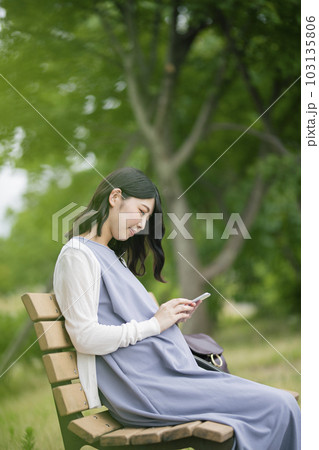 公園でスマートフォンを見る妊婦 公園でスマートフォンを見る妊婦 103135806