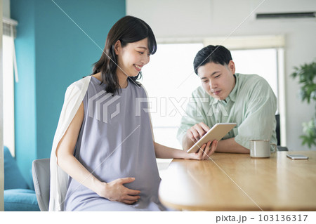 リビングで一緒にタブレット端末を見る若い夫婦 103136317
