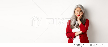 Troubled and sad asian female entrepreneur looking at upper left corner, thinking with upset face, standing over white background 103140530