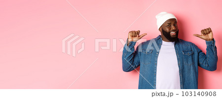 Confident Black bearded man in hipster beanie and denim shirt, pointing at himself with self-assured face, standing over pink background 103140908