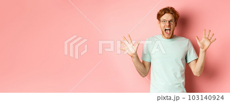 Angry and pressured young man losing temper, spread hands sideways and screaming with furious face, standing in glasses and t-shirt against pink background Angry and pressured young man losing temper, spread hands sideways and screaming with furious face, standing in glasses and t-shirt against pink background 103140924