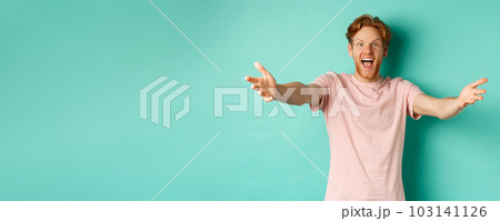Friendly and happy young man with ginger hair, stretch out hands in warm welcome, reaching for hug and smiling joyfully, standing in t-shirt over mint background Friendly and happy young man with ginger hair, stretch out hands in warm welcome, reaching for hug and smiling joyfully, standing in t-shirt over mint background 103141126