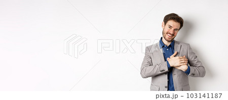 Happy man in suit holding hands on heart, feeling touched or grateful, having tender memories in soul, standing against white background 103141187