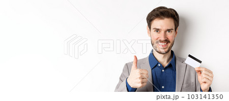 Shopping. Handsome satisfied client showing thumbs up and plastic credit card, smiling pleased, white background Shopping. Handsome satisfied client showing thumbs up and plastic credit card, smiling pleased, white background 103141350