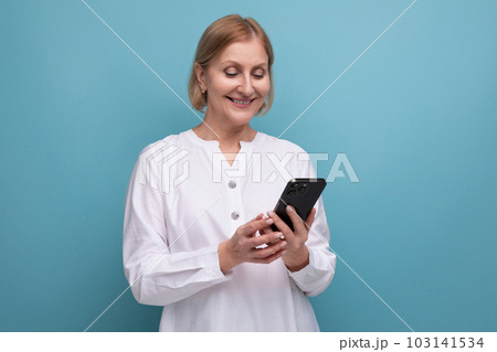 healthy slim blond mature woman mastering technique using smartphone on studio background 103141534