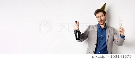 Celebration and holidays concept. Happy man in suit having fun at party, wearing birthday hat, dancing with champagne and drinking alcohol Celebration and holidays concept. Happy man in suit having fun at party, wearing birthday hat, dancing with champagne and drinking alcohol 103141679