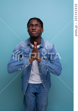 portrait of a young cheerful american man with dreadlocks in a denim jacket praying 103141916